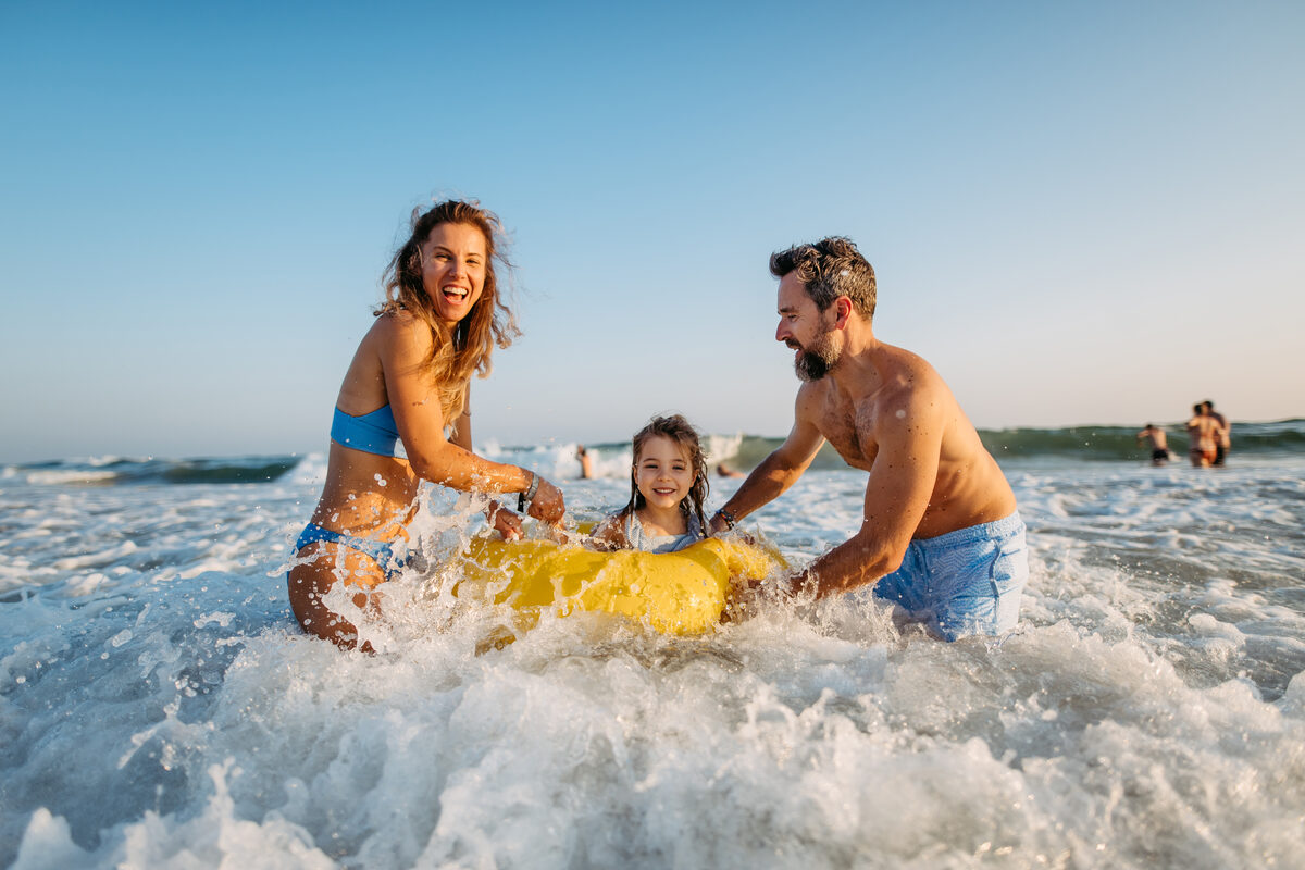 A family laughing together while riding a wave at the beach