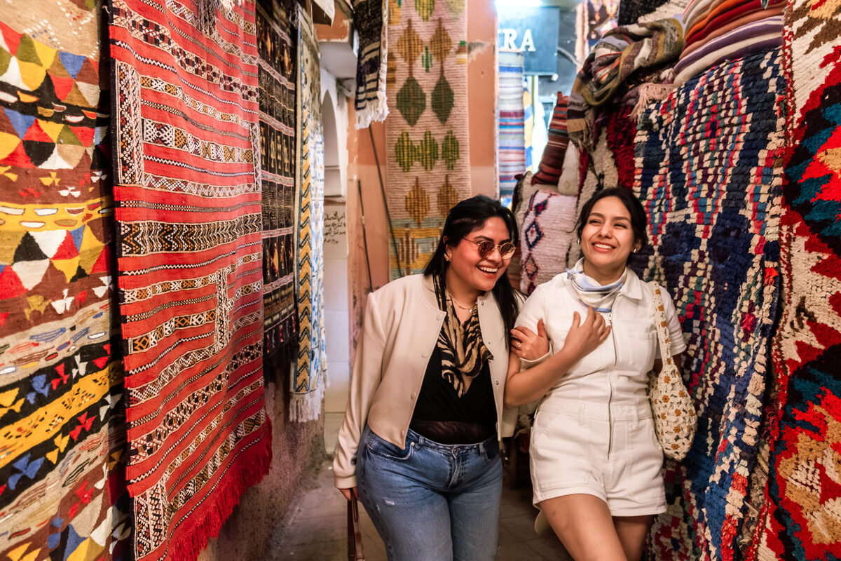 Two young women laughing as they explore a colorful Marrakech market